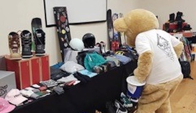 person in a bear costume sat on a red leather chair with snowboards on the wall behind