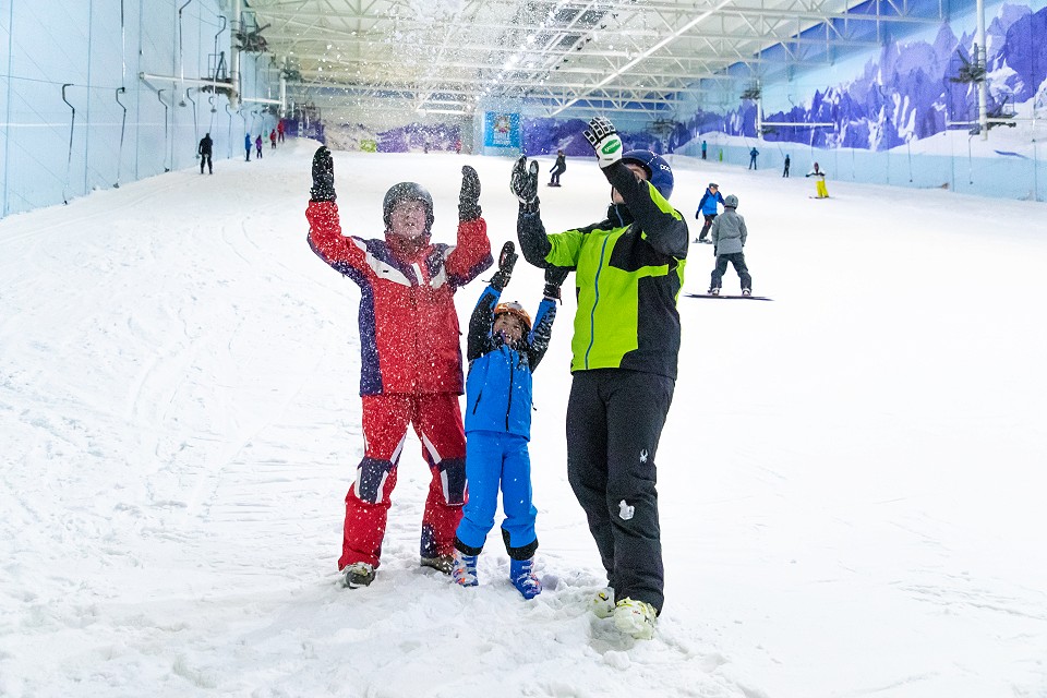 family having fun in the snow with their arms in the air and smiles on their face