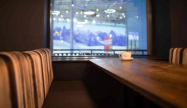 White cup and saucer with red writing, on a wooden table with snowy peaks on the wall in the back