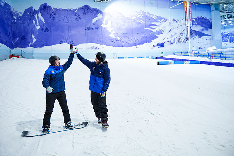 Chill Factor<sup>e</sup> snowsports instructor high fiving a snowboarder at indoor ski slope