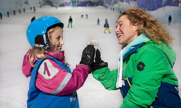 Woman and young child stood in the snow, they are smiling at eachother and touching hands.