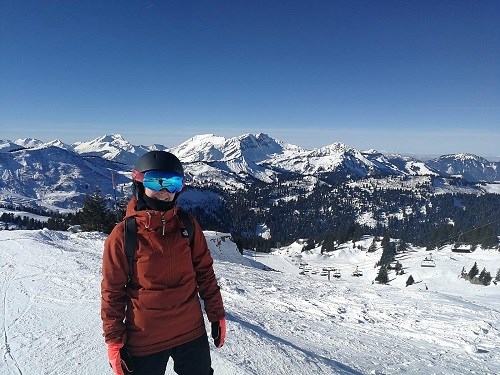 A person stood in red snow clothing, behind them is a mountain range with snowy peaks