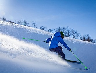 Skier wearing a blue jacket skiing down a mountain, spraying snow.