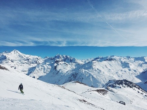 A range of snowy mountains with a blue sky in the background, their is a skier riding down the slope