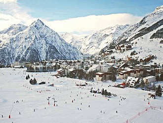 View of a ski village, in the foreground is a group of skiers, there are mountains in the background