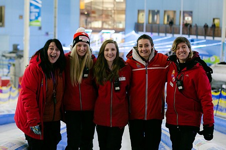 Group of five adults, all smiling with their arms round each other, one is wearing a bobble hat.