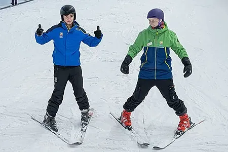 Ski instructor demonstrating the snow plough technique to learner skier.